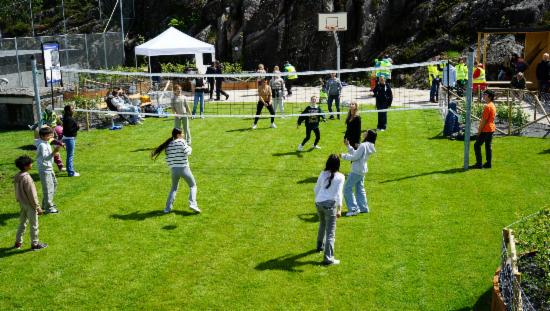 Barn spiller volleyball på grønt gress, sol og basketballkurv i bakgrunnen. 