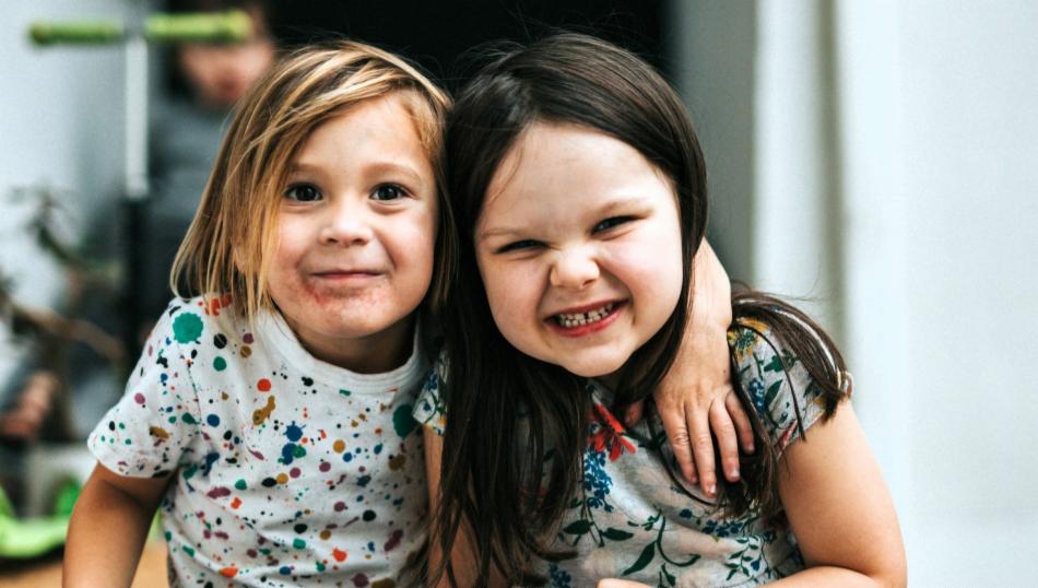 To små jenter holder rundt hverandre ogsmiler til kamera