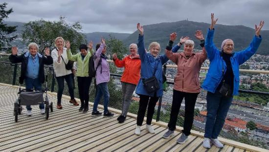 En stor gjeng med pensjonister står smilende på den nye gangbroen på Løvstien